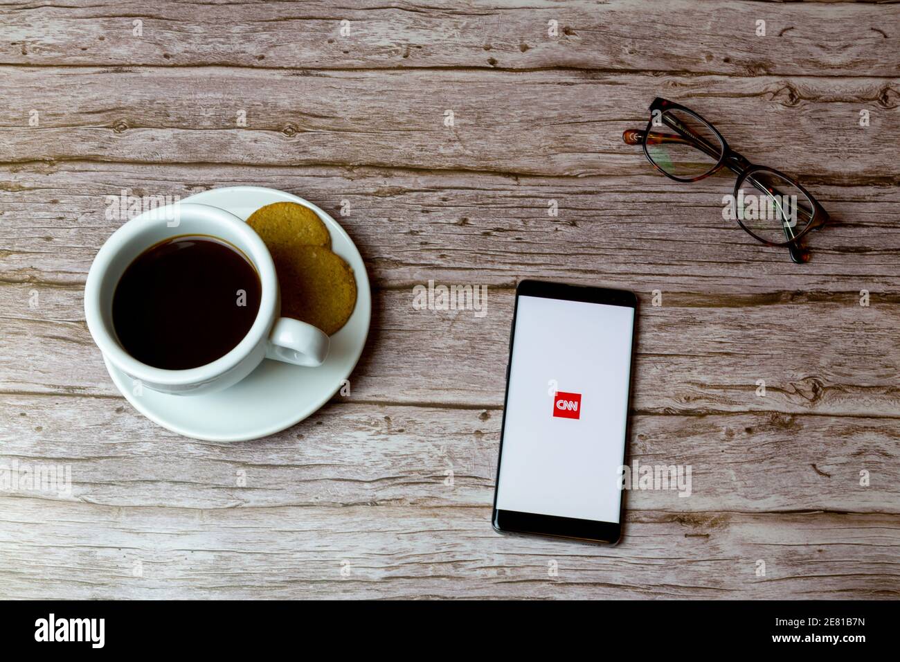 Ein Handy oder Handy auf einem Holz gelegt Tisch mit der CNN News App Eröffnung auch einen Kaffee Und Brille Stockfoto