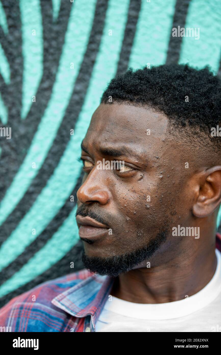 Ein schwarzer Mann steht vor einer türkis-schwarz bemalten Wand. Stockfoto