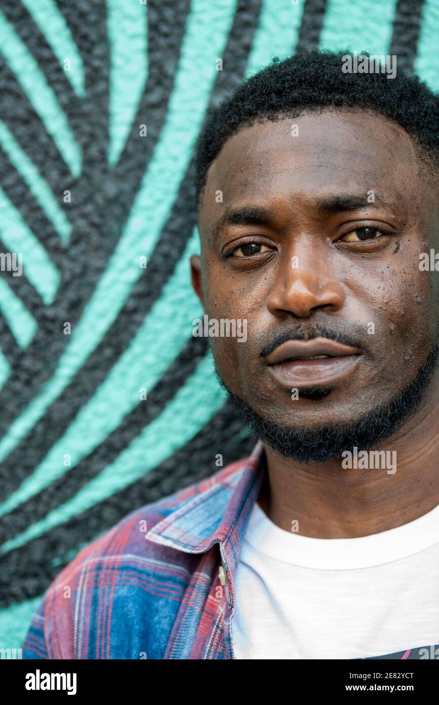 Ein schwarzer Mann steht vor einer türkis-schwarz bemalten Wand. Stockfoto