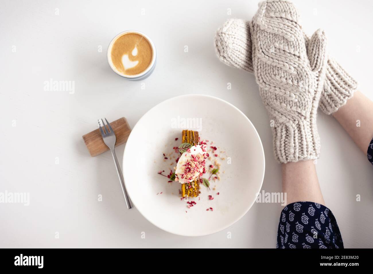 Weibliche Hände in weißen Fäustlingen mit Kuchen und Kaffee auf weißem Tisch mit Kuchen. Konzept von Winter, Wärme, Urlaub, Veranstaltungen. Stockfoto