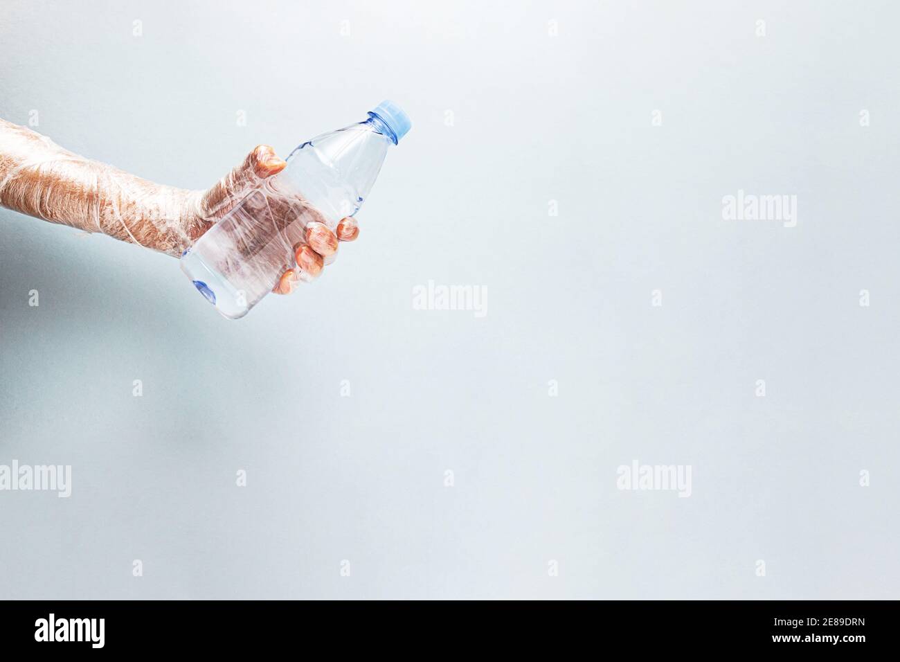 Kein Kunststoffkonzept. Eine Hand in Plastikfolie eingewickelt hält eine Plastikwasserflasche. Stockfoto