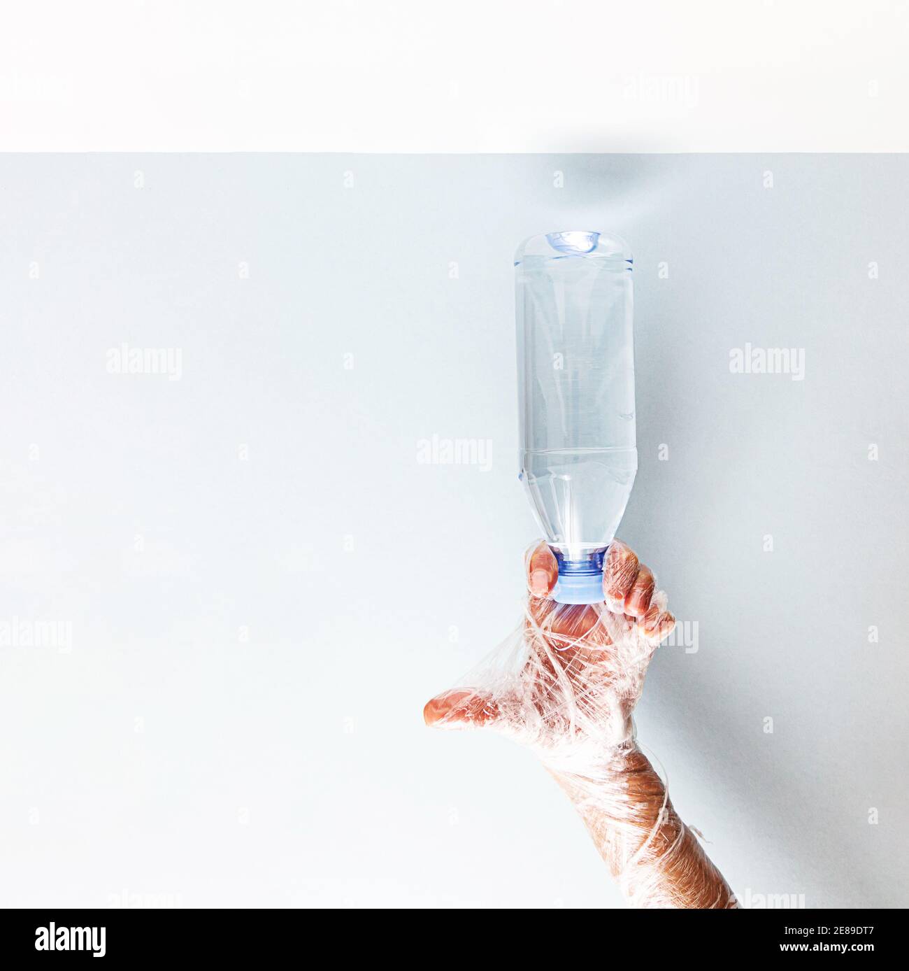 Kein Kunststoffkonzept. Eine Hand in Plastikfolie eingewickelt hält eine Plastikwasserflasche. Stockfoto