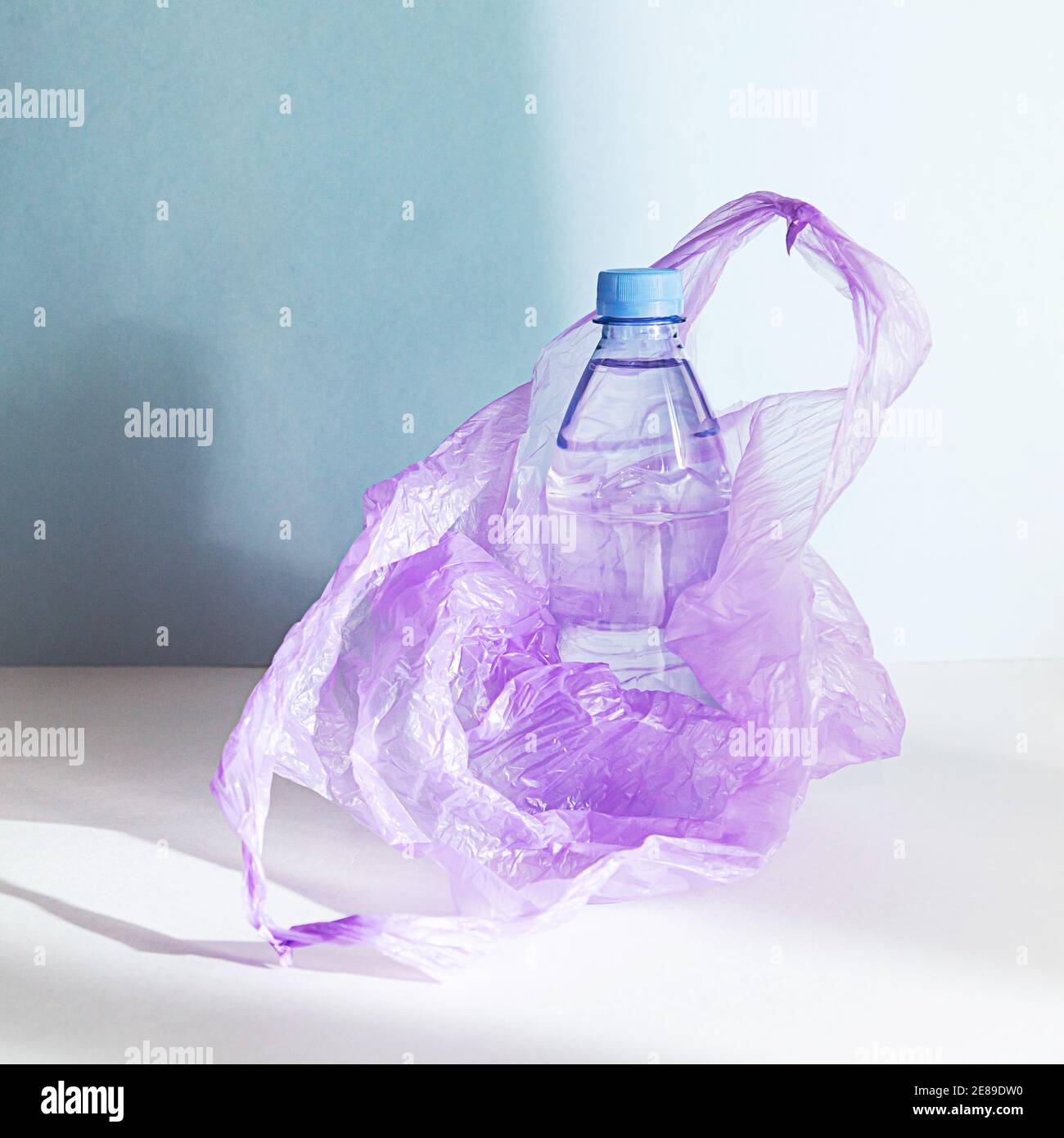 Eine Plastikwasserflasche in einem Plastikbeutel, die darauf wartet, recycelt zu werden. Kein minimales Plastikkonzept auf blauem Hintergrund mit Schatten. Stockfoto