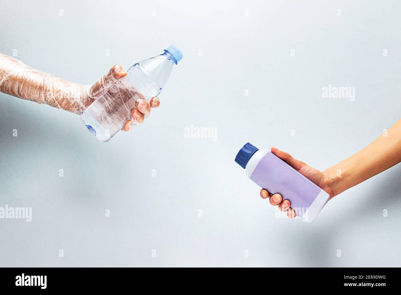 Eine Plastikwasserflasche in der Hand in Polyethylen verpackt und eine wiederverwendbare Wasserflasche in der anderen Hand. Kein Kunststoffkonzept. Stockfoto