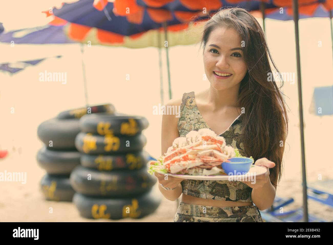 Junge glücklich schöne asiatische Frau lächelnd, während Sie die Platte aus gedämpftem frisch Krabben am öffentlichen Strand von Hua Hin in Thailand gekocht Stockfoto