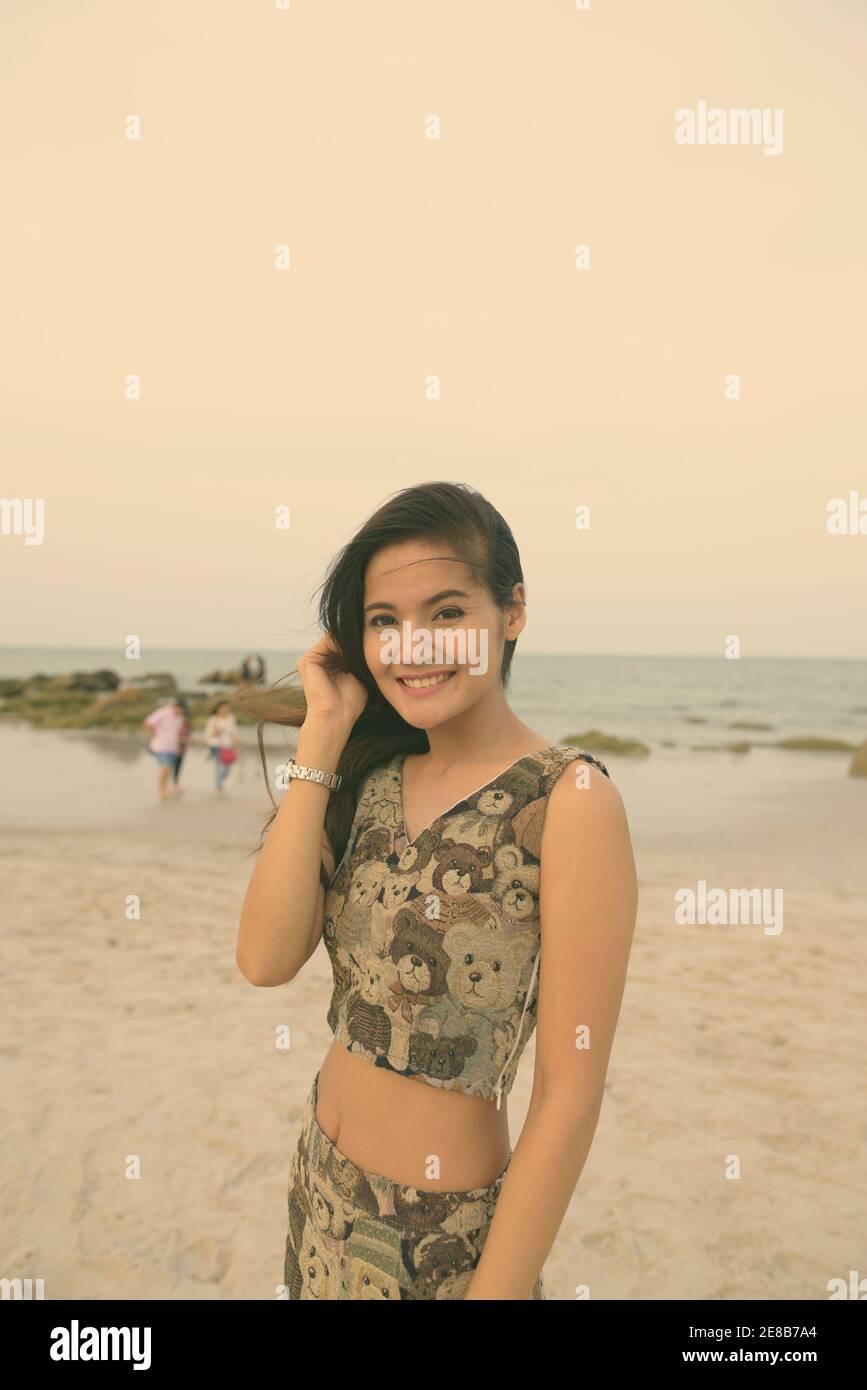 Junge asiatische Frau glücklich lächelnd, während sie ihr Haar am öffentlichen Strand von Hua Hin in Thailand zur Festsetzung Stockfoto