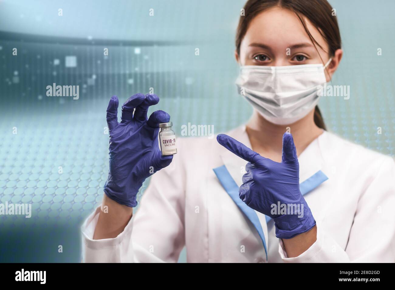 Eine Glasflasche mit dem Coronavirus-Impfstoff. Eine Ampulle mit einem Impfstoff in der Hand eines jungen Arztes auf blauem abstrakten Hintergrund Stockfoto