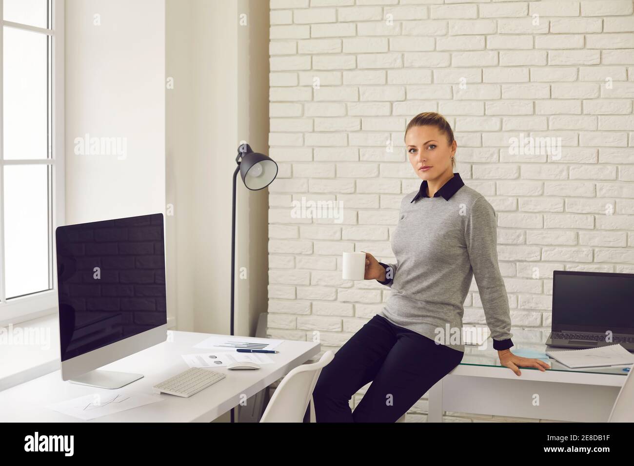 Junge Büroangestellte, die mit Kaffee am Schreibtisch sitzt Stockfoto