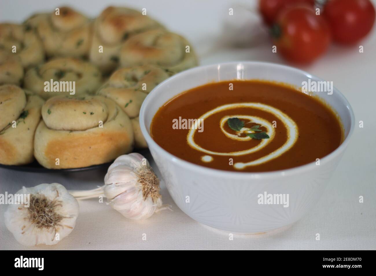 Hausgemachte gesunde Tomatensuppe gepaart mit frisch gebackenem Abendessen Brötchen mit Knoblauchbutter und italienischem Kraut Stockfoto