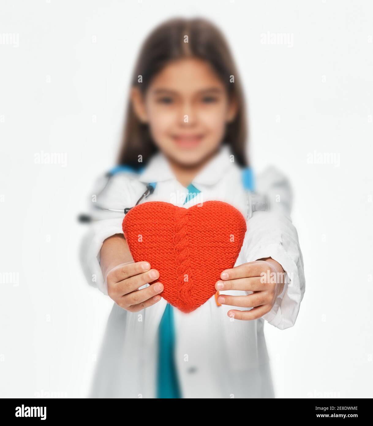 Weibliches Kind, das einen medizinischen Mantel trägt, der die Form eines Herzens vor sich hält. Konzept für die Gesundheit des Kindes im Herzen. Weichfokus Stockfoto