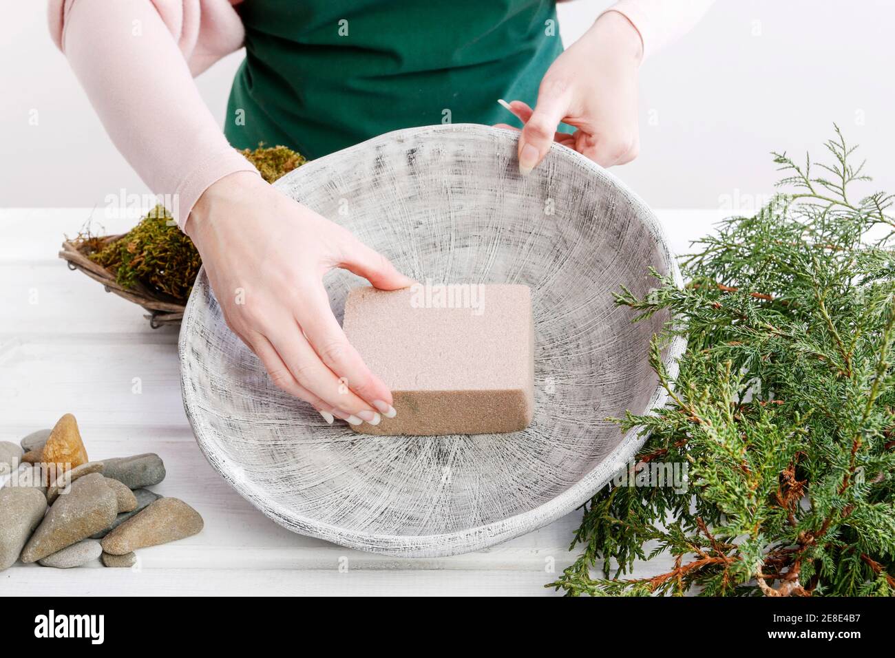 Floristin bei der Arbeit: Frau zeigt, wie man kleinen weihnachtsbaum mit einem Nadelstrauchzweig, Steinen und Moos macht. Schritt für Schritt, Tutorial. Stockfoto