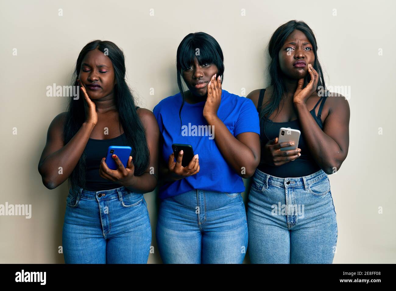 Drei junge afroamerikanische Freunde mit Smartphone berühren Mund mit Hand mit schmerzhaftem Ausdruck aufgrund von Zahnschmerzen oder Zahnerkrankungen Auf den Zähnen Stockfoto