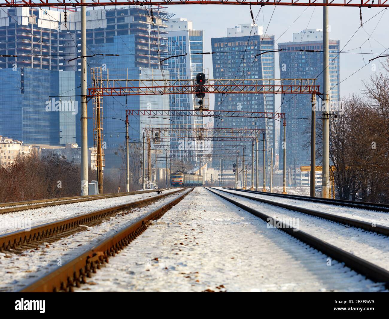 Der Elektrozug bewegt sich auf Schienen vor dem Hintergrund einer winterlichen Stadtlandschaft aus Wolkenkratzern, zentraler Perspektive, Kopierraum. Stockfoto