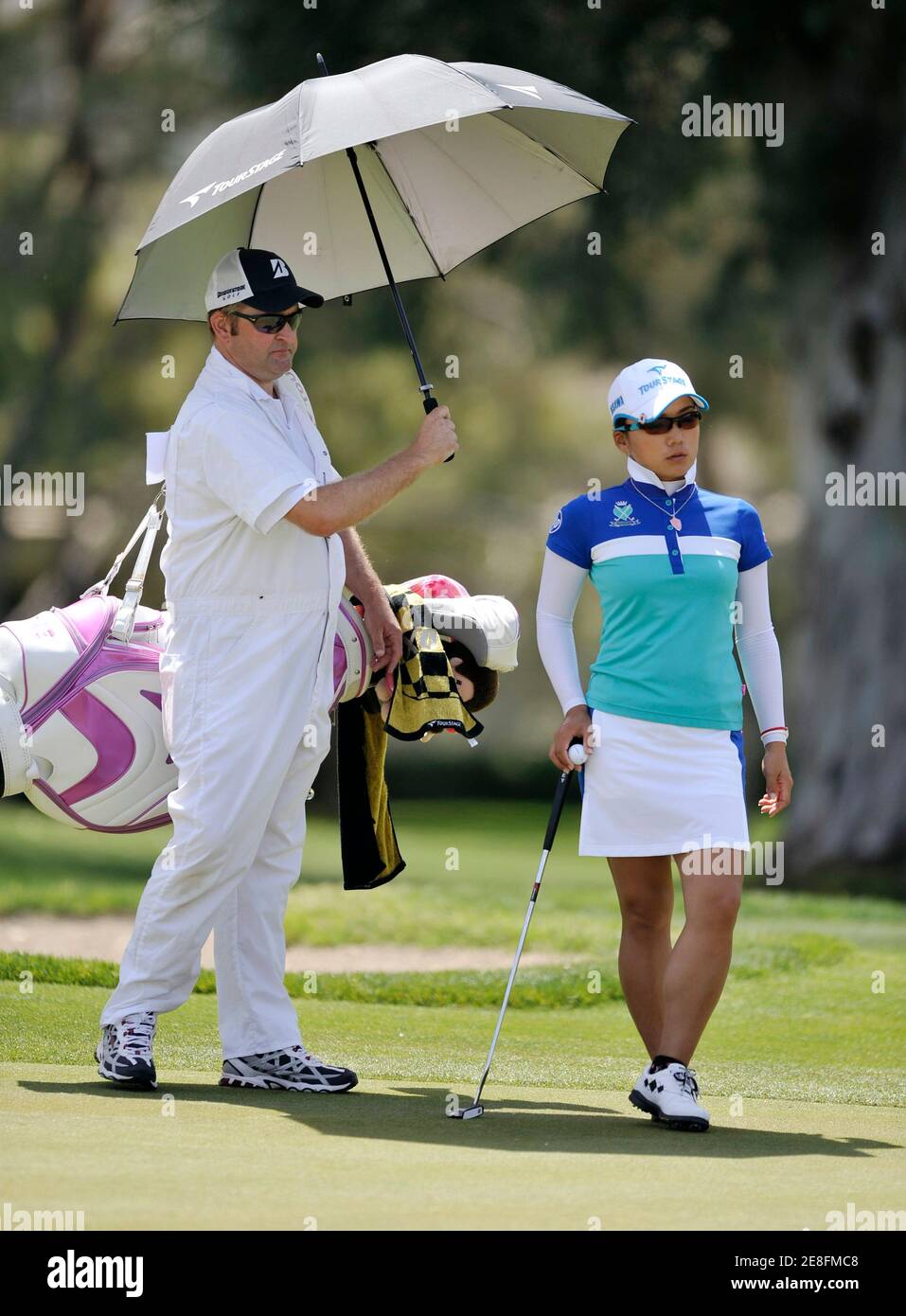 Chie Arimura (R) von Japan wird von ihr Caddie mit einem Regenschirm beschattet, während sie darauf wartet, Putten auf dem vierten Loch während der dritten Runde Wiedergabe der LPGA ist Kraft Nabisco Women Golf-Meisterschaft in Rancho Mirage, Kalifornien 3. April 2010.  REUTERS/Gus Ruelas (Vereinigte Staaten - Tags: SPORT-GOLF) Stockfoto