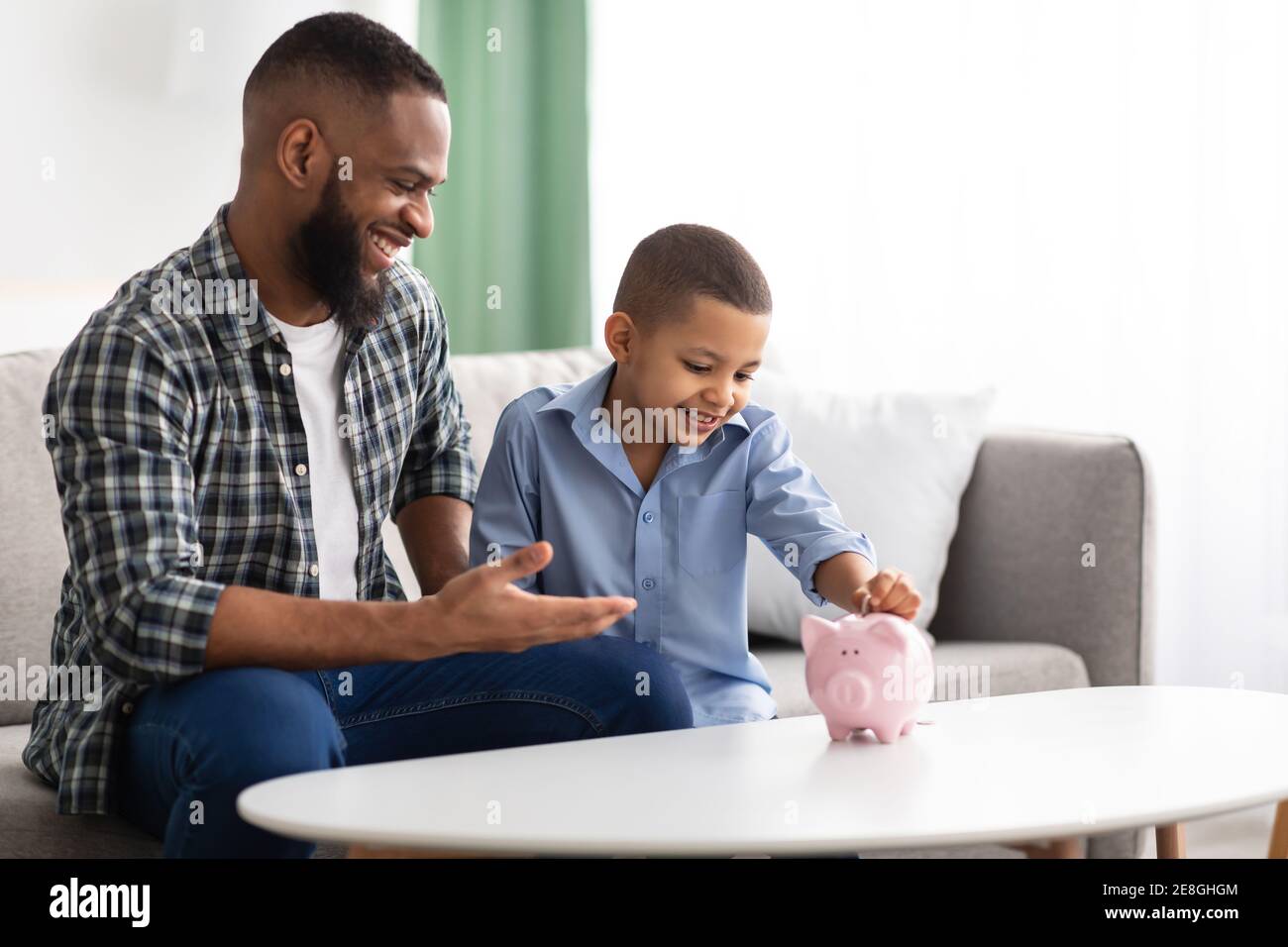 African Vater Und Sohn Putting Persönliche Ersparnisse In Piggybank Indoor Stockfoto