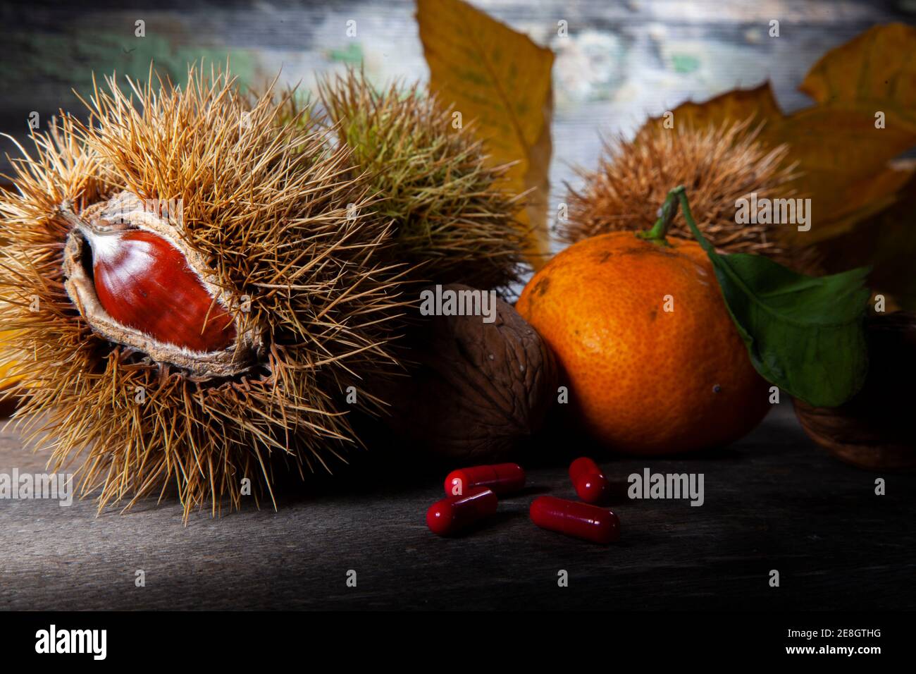 Herbst Stillleben von Kastanie, Mandarine und Pillen. Makrofoto von auf Holztisch mit verfallener Hintergrund. Aufgenommen mit Spotlight in Studio Stockfoto
