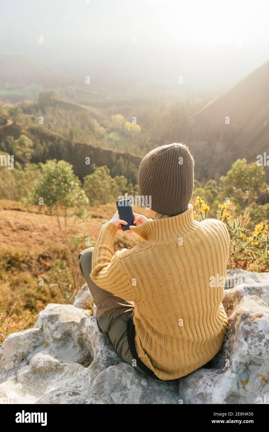 Rückansicht von weiblichen Explorer Messaging auf Handy während Sitzen auf dem Hintergrund der Bergkette an sonnigen Tag Stockfoto