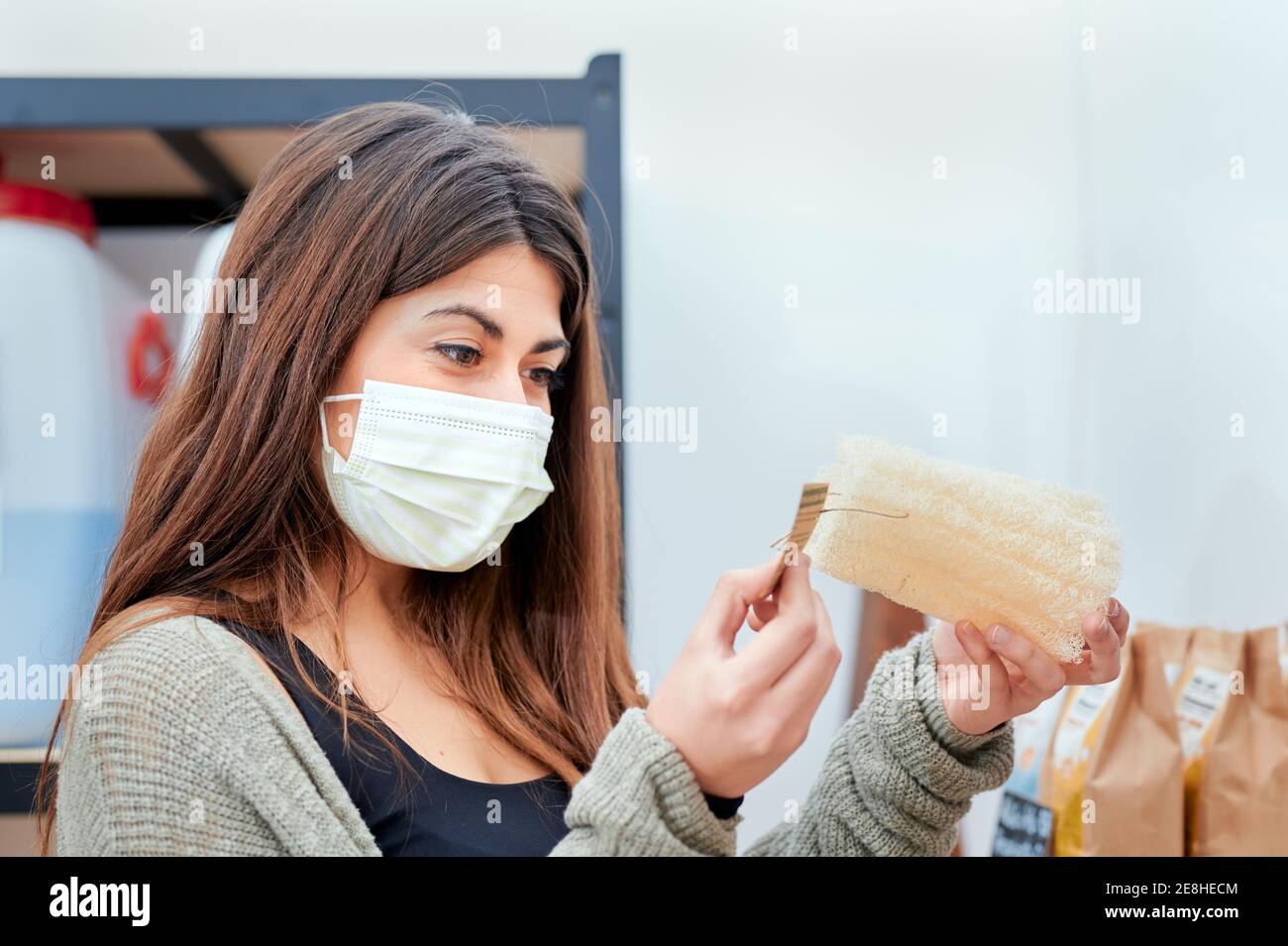 Seitenansicht des weiblichen Klienten in der medizinischen Maske, die Informationen liest Auf Papier Preisschild beim Einkaufen in Großlager Stockfoto