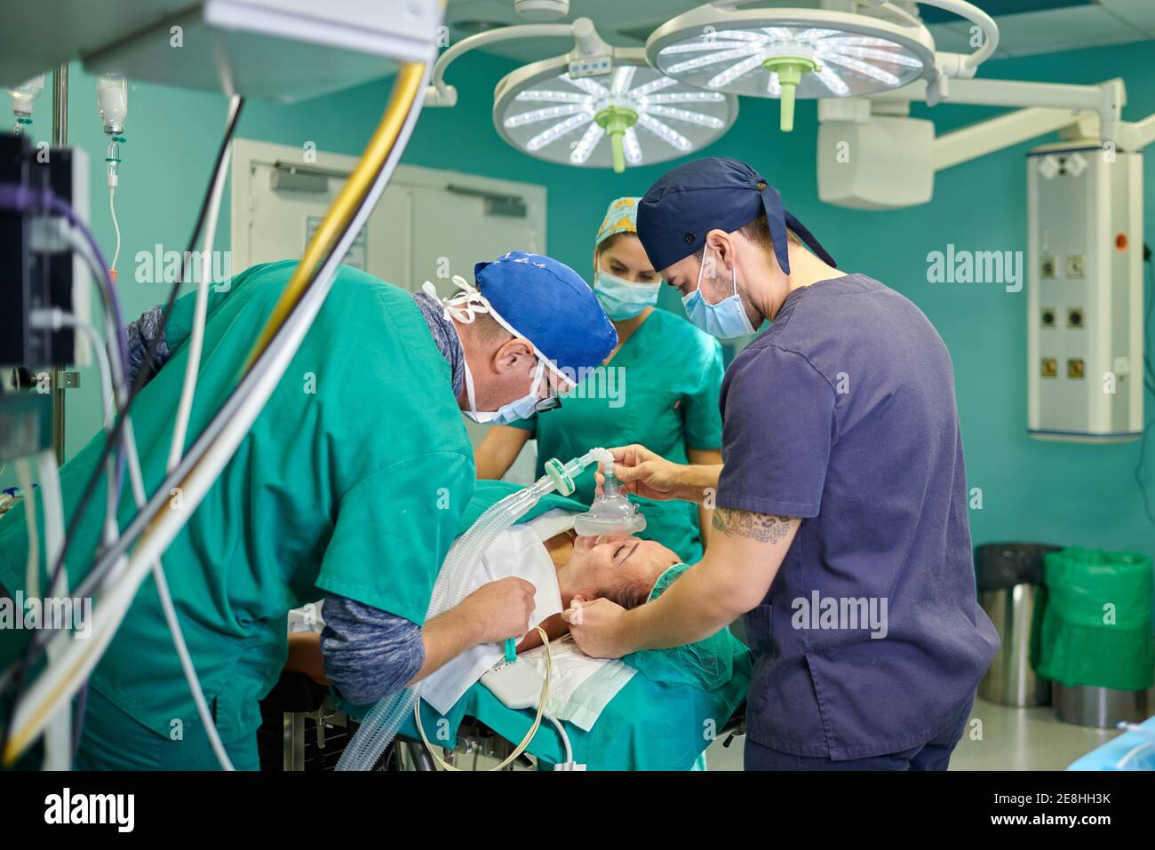 Seitenansicht des anonymen männlichen Anästhesisten in medizinischen Uniform und Kappe hält Anästhesiemaske auf Gesicht von nicht erkennbaren Patienten liegend Auf dem Tisch im OP Stockfoto