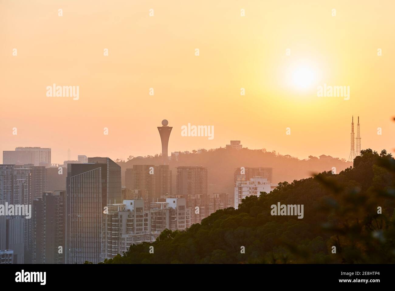 Friedlicher Blick auf die moderne Metropole mit Wolkenkratzern und Wohngebäuden Unter orangefarbenem Himmel in der Dämmerung Stockfoto