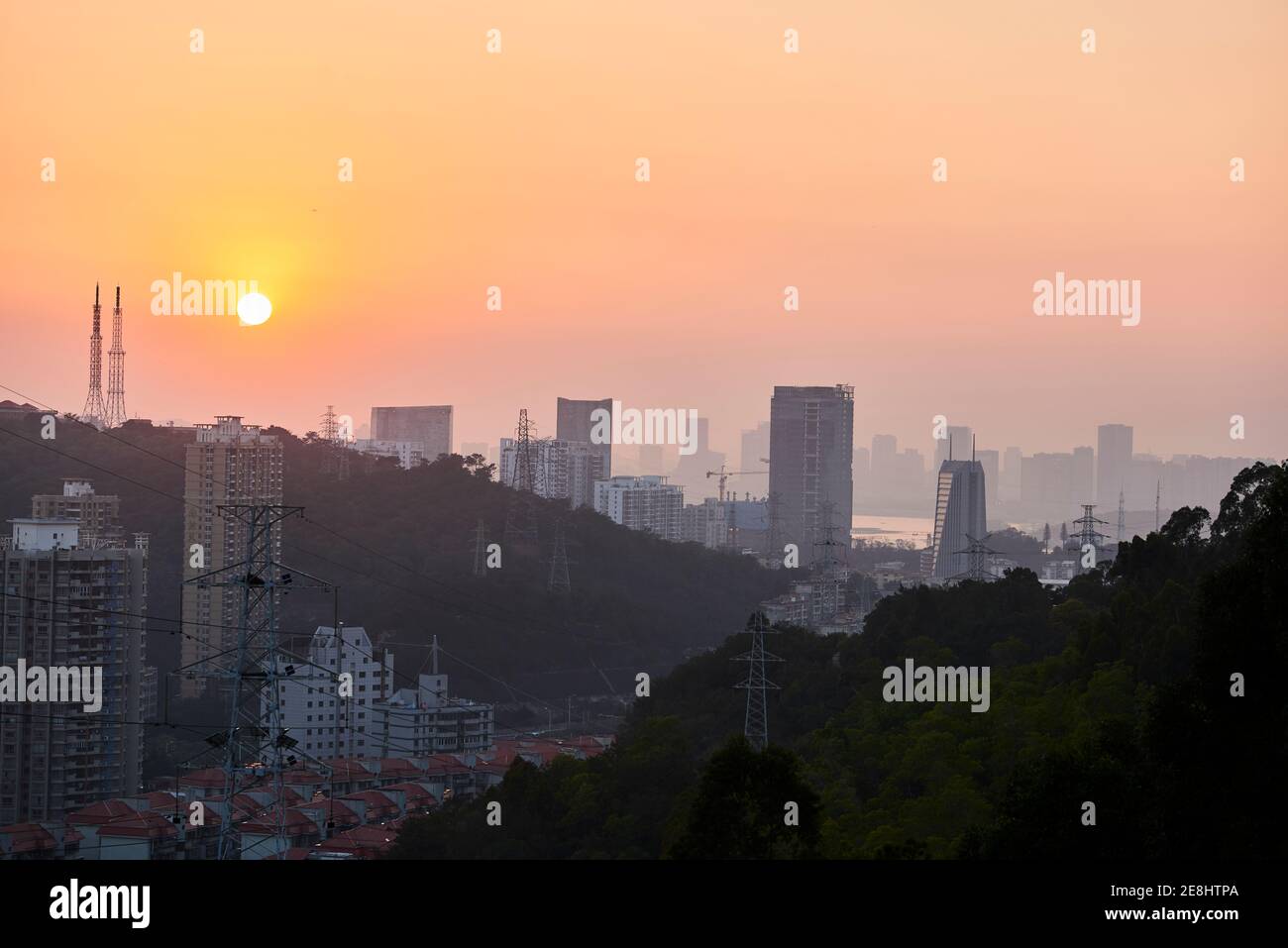 Friedlicher Blick auf die moderne Metropole mit Wolkenkratzern und Wohngebäuden Unter orangefarbenem Himmel in der Dämmerung Stockfoto
