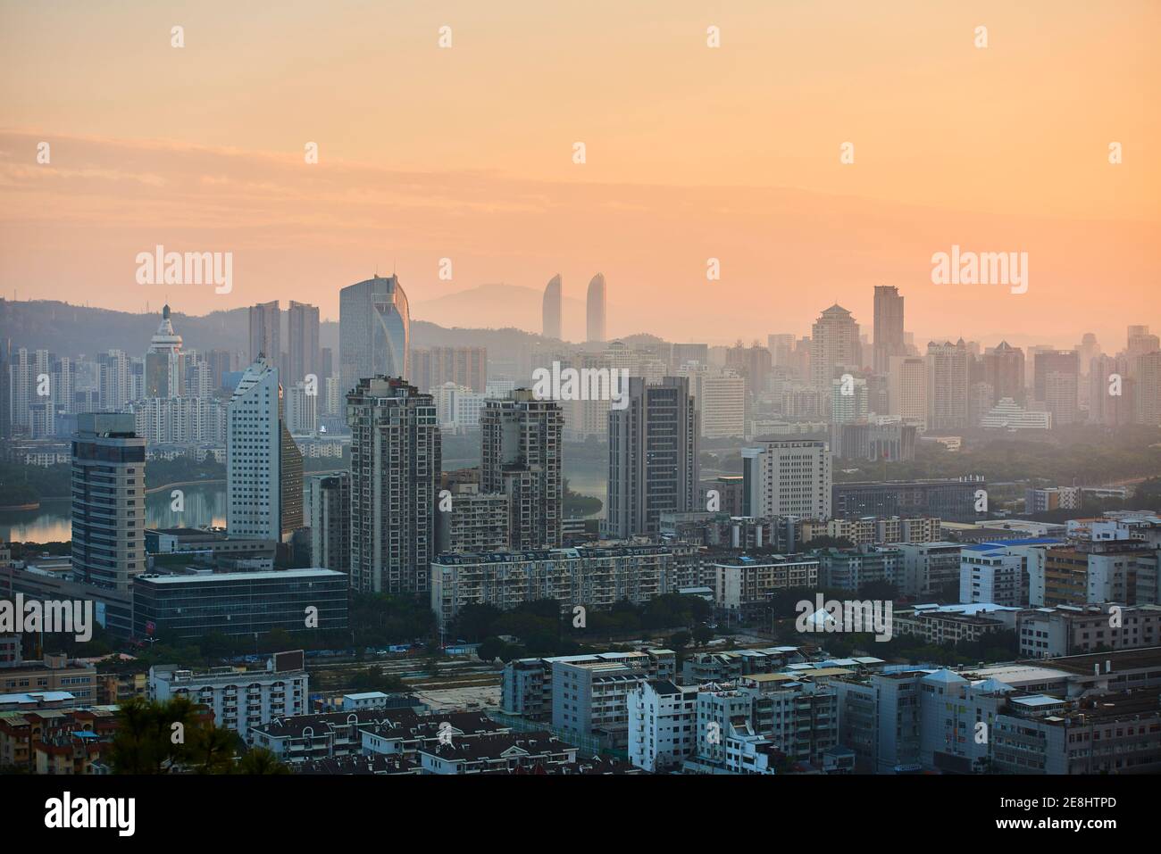Friedlicher Blick auf die moderne Metropole mit Wolkenkratzern und Wohngebäuden Unter orangefarbenem Himmel in der Dämmerung Stockfoto