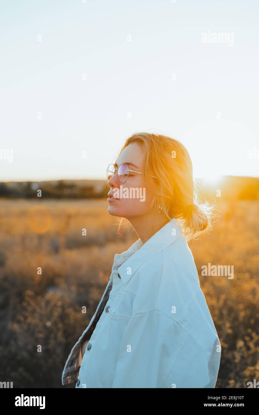 Side vie von trendigen jungen weiblichen Touristen mit blonden Haaren In legerer Kleidung und Brillen auf der Landstraße inmitten spazieren Trockene Pflanzen auf dem Land Stockfoto