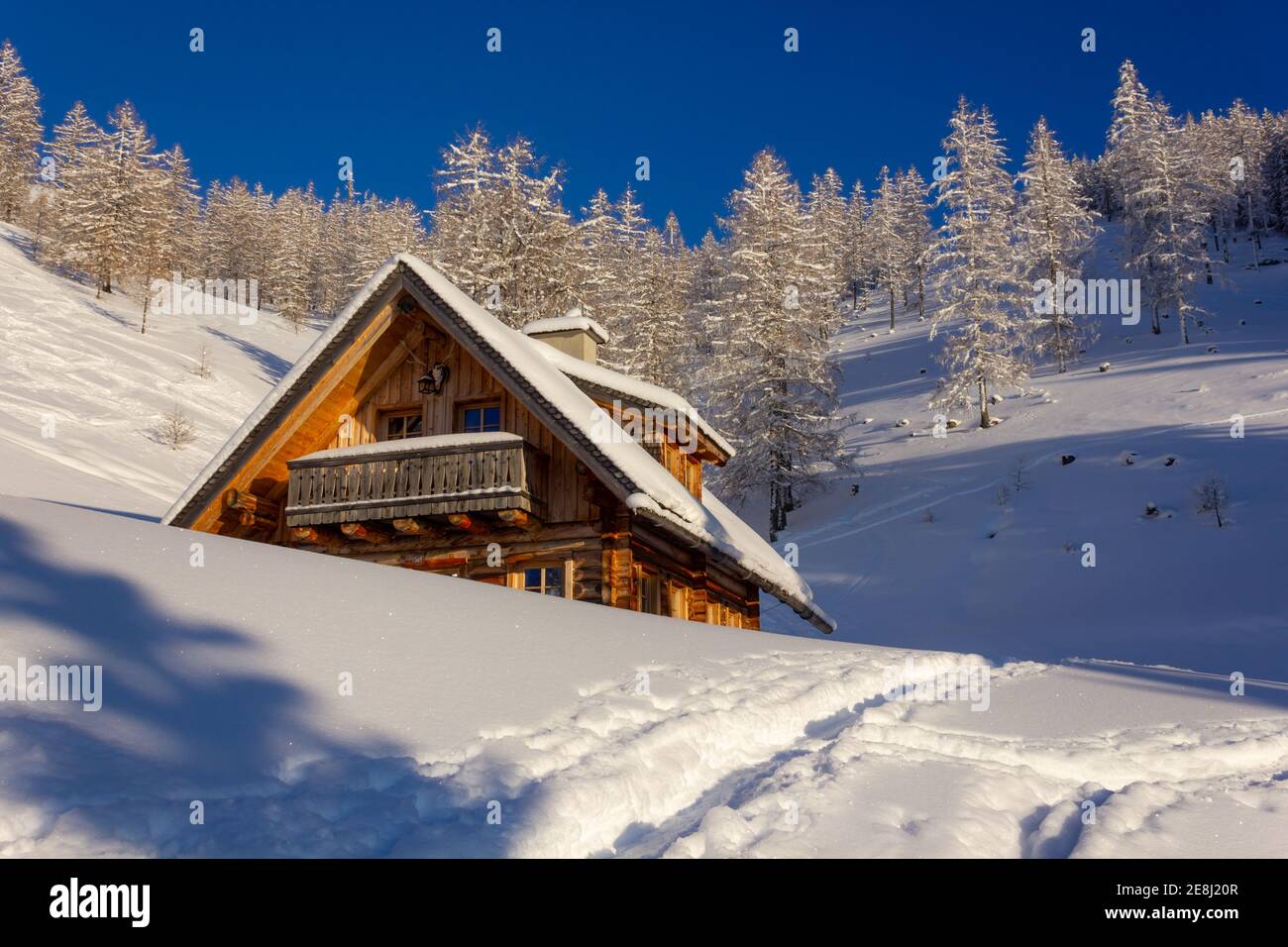 Gefrorene Landschaft mit österreichischer Blockhütte und verschneiten Lärchenbäumen Im Hintergrund Stockfoto