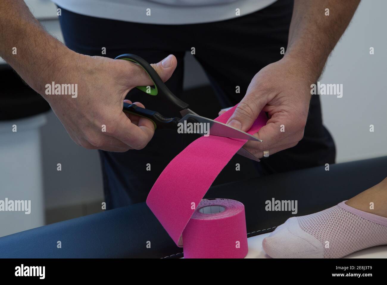 Crop männlichen Physiotherapeuten in sterile Maske Schneiden elastische Kinesiologie Klebeband mit Schere im Krankenhaus Stockfoto