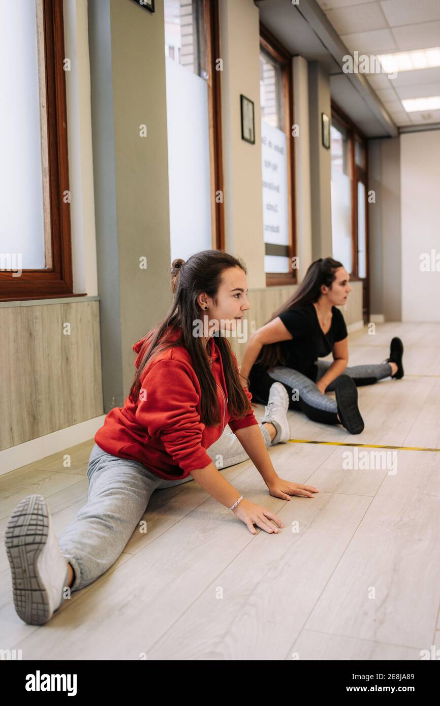 Lächelnd weibliche Trainer in Sportbekleidung helfen fröhliche Mädchen mit Stretching Beine beim Aufwärmen vor dem Fitnesstraining Stockfoto