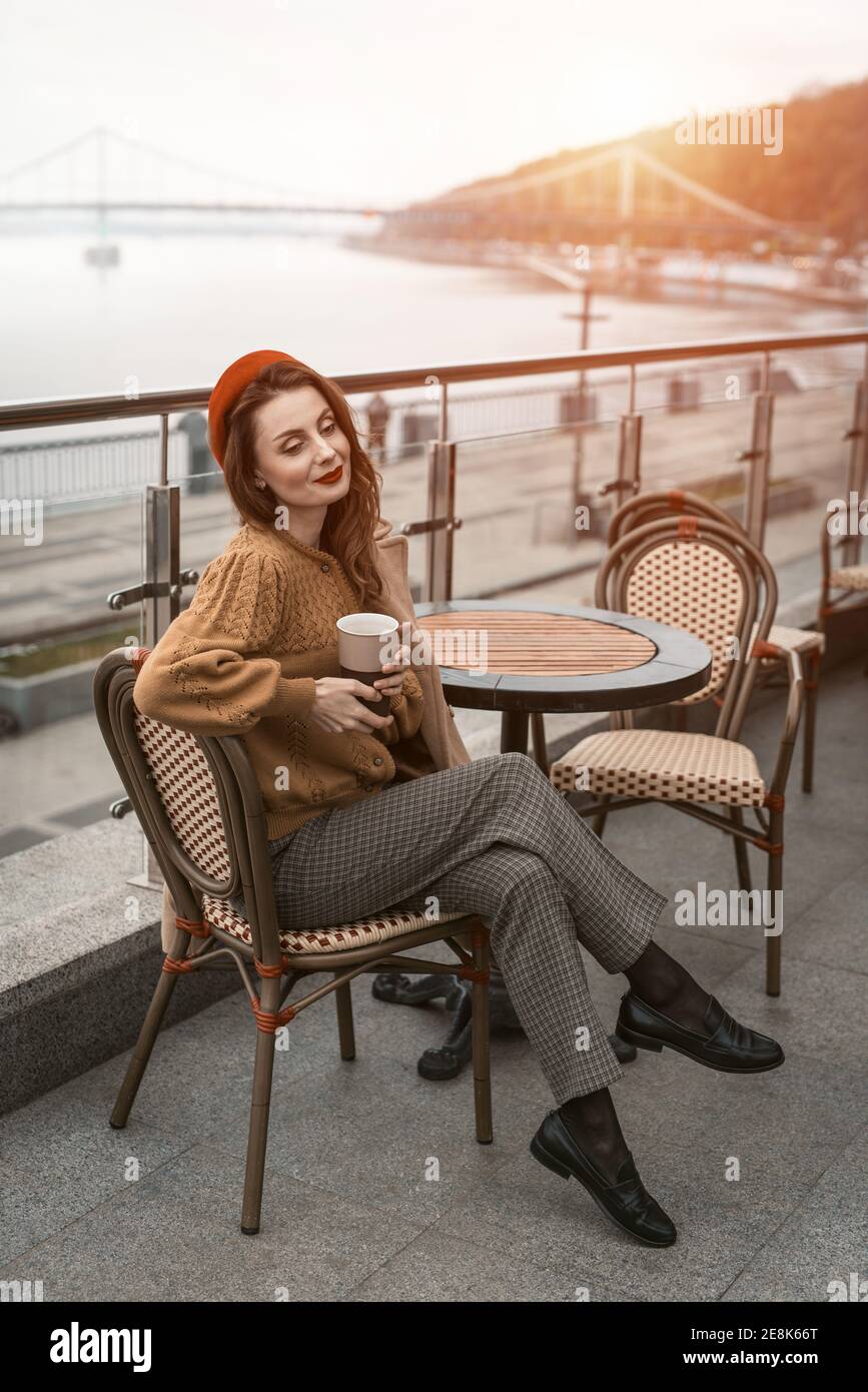 Charmante Frau genießen ihre Tasse Kaffee in einem Frühling im Freien Café sitzen. Französisch Frau in roten Baskenmütze mit Hintergrund der Stadt. Pariser Frau Stockfoto