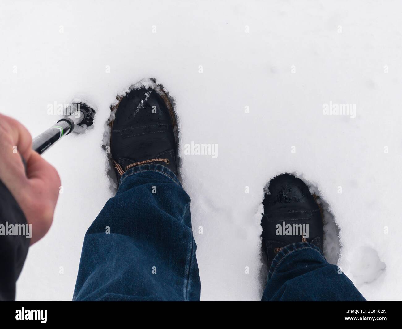 Draufsicht auf menschliche Stiefel, die im tiefen Schnee stehen Zu Fuß Stick, dass die Hand fest nehmen Stockfoto