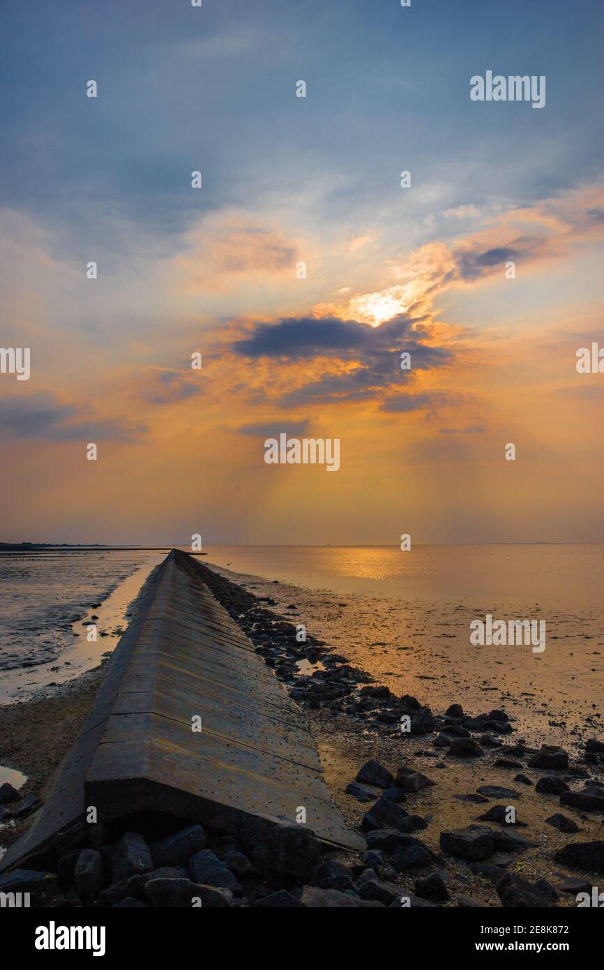 Bei Ebbe geht die Sonne über dem wattenmeer unter Aufdeckung eines konkreten Küstenschutzes Stockfoto