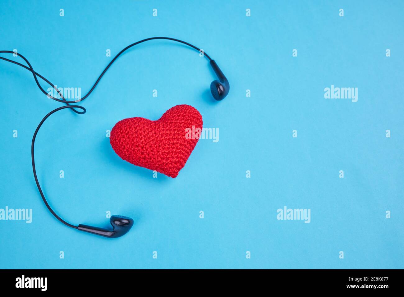 Schwarze Ohrhörer in der Nähe roten Herzen über blauem Hintergrund mit Kopierraum. Liebe zur Musik Rhythmus Konzept Stockfoto