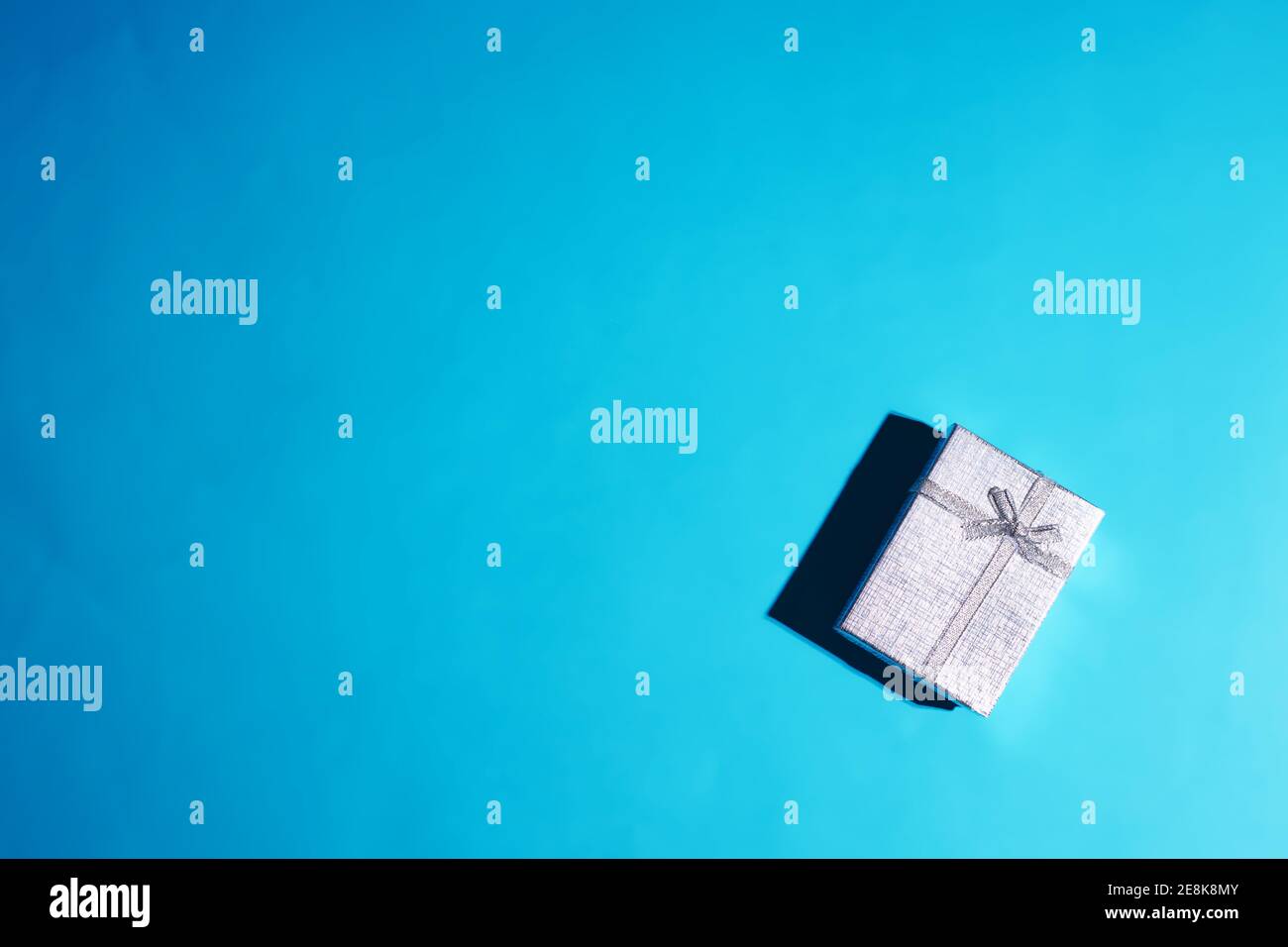 Silberfarbene Geschenkbox isoliert auf einem blauen Hintergrund mit Kopierraum. Harter Schatten Stockfoto