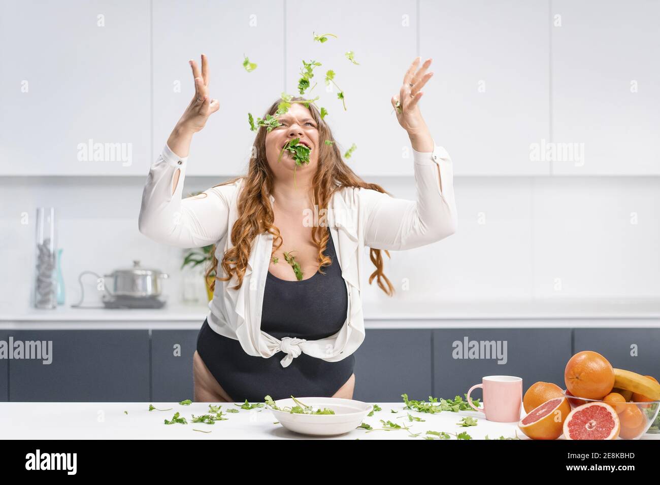 Glücklich mollige Mädchen Streuung Spinat Blätter über den Tisch. Übergewichtige Mädchen glücklich Gewicht zu verlieren Essen frischen Salat. Kurvige Körper junge Frau mit Stockfoto