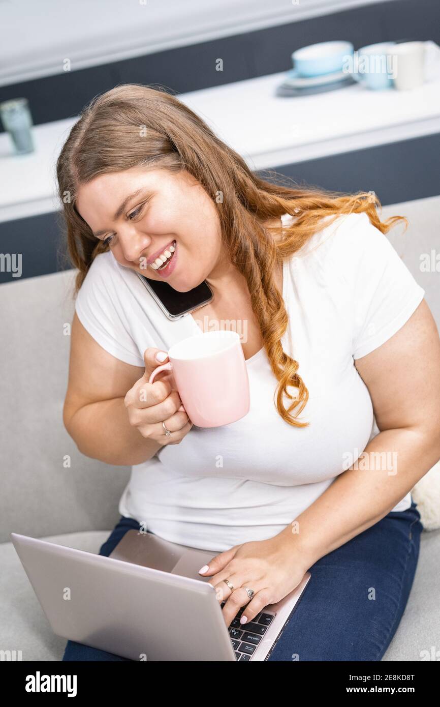 Trinken Kräutertee Gespräch am Telefon mit Ernährungsberater Blick auf das Programm auf einem Laptop junge fette Mädchen zu Hause bleiben während der Quarantäne. Selbst Stockfoto