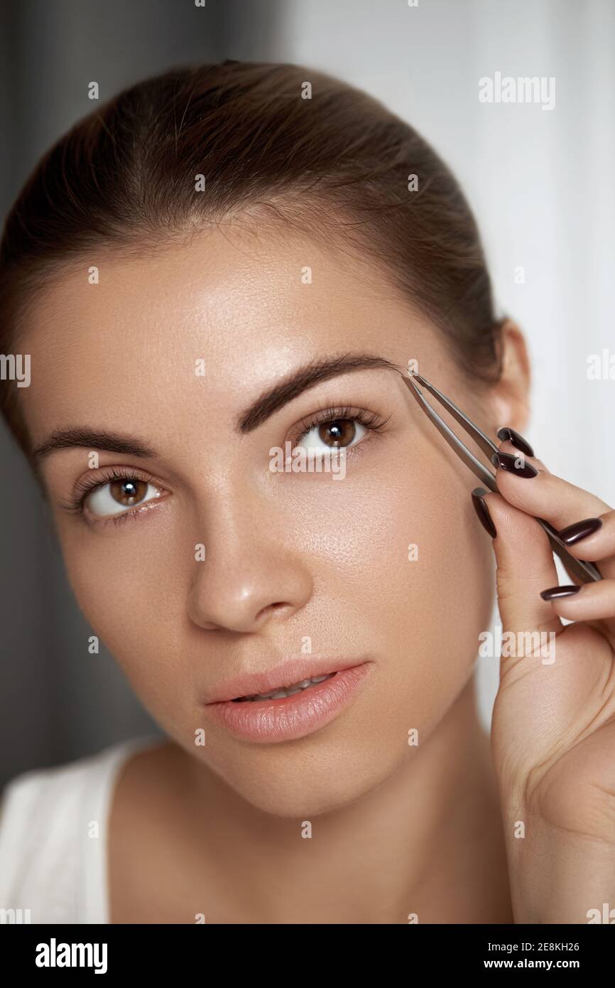 Augenbrauenkorrektur. Augenbrauen zupfen. Schöne junge Frau mit Pinzette. Modell mit Beauty-Gesicht. Stockfoto