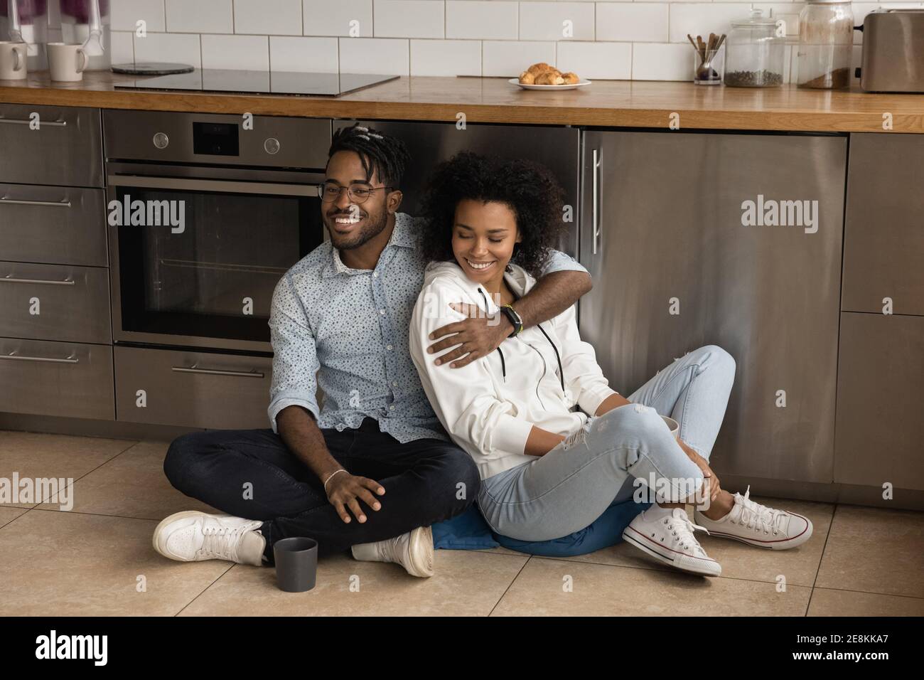Liebevolle glückliche afrikanische Ehegatten kuscheln auf dem Boden in der modernen Küche Stockfoto