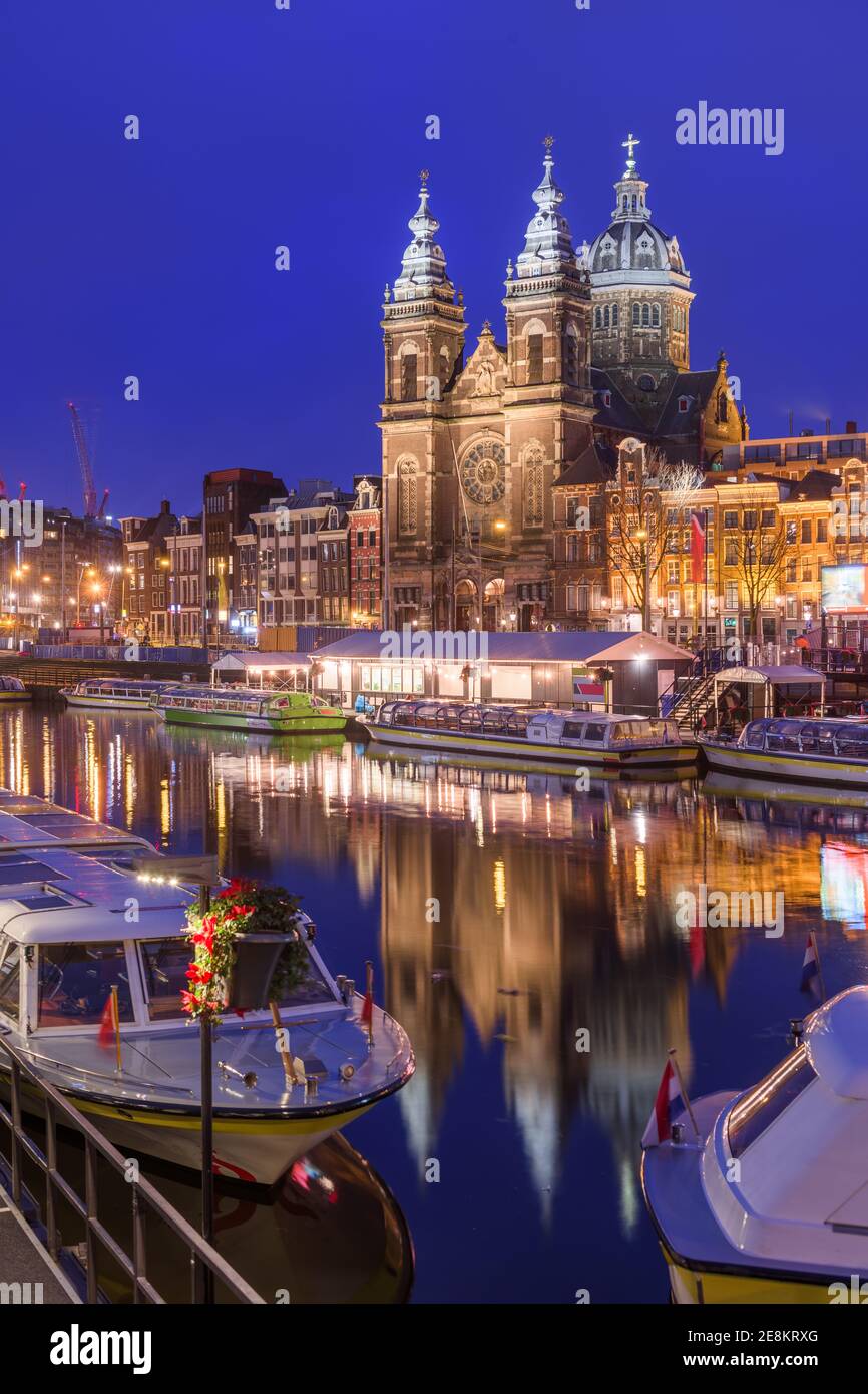 Amsterdam, Niederlande Blick ins Stadtzentrum mit Flussbooten und der Basilika St. Nikolaus bei Nacht. Stockfoto
