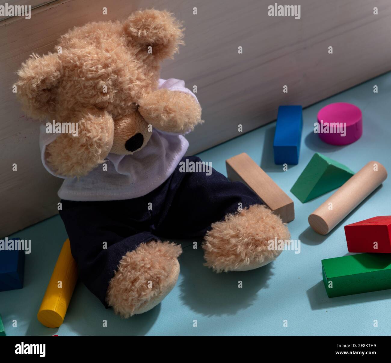 Konzept für Kindesmissbrauch. Teddybär bedeckt die Augen, sitzt auf dem Boden des Kinderzimmers, bunte Holzblöcke herum Stockfoto