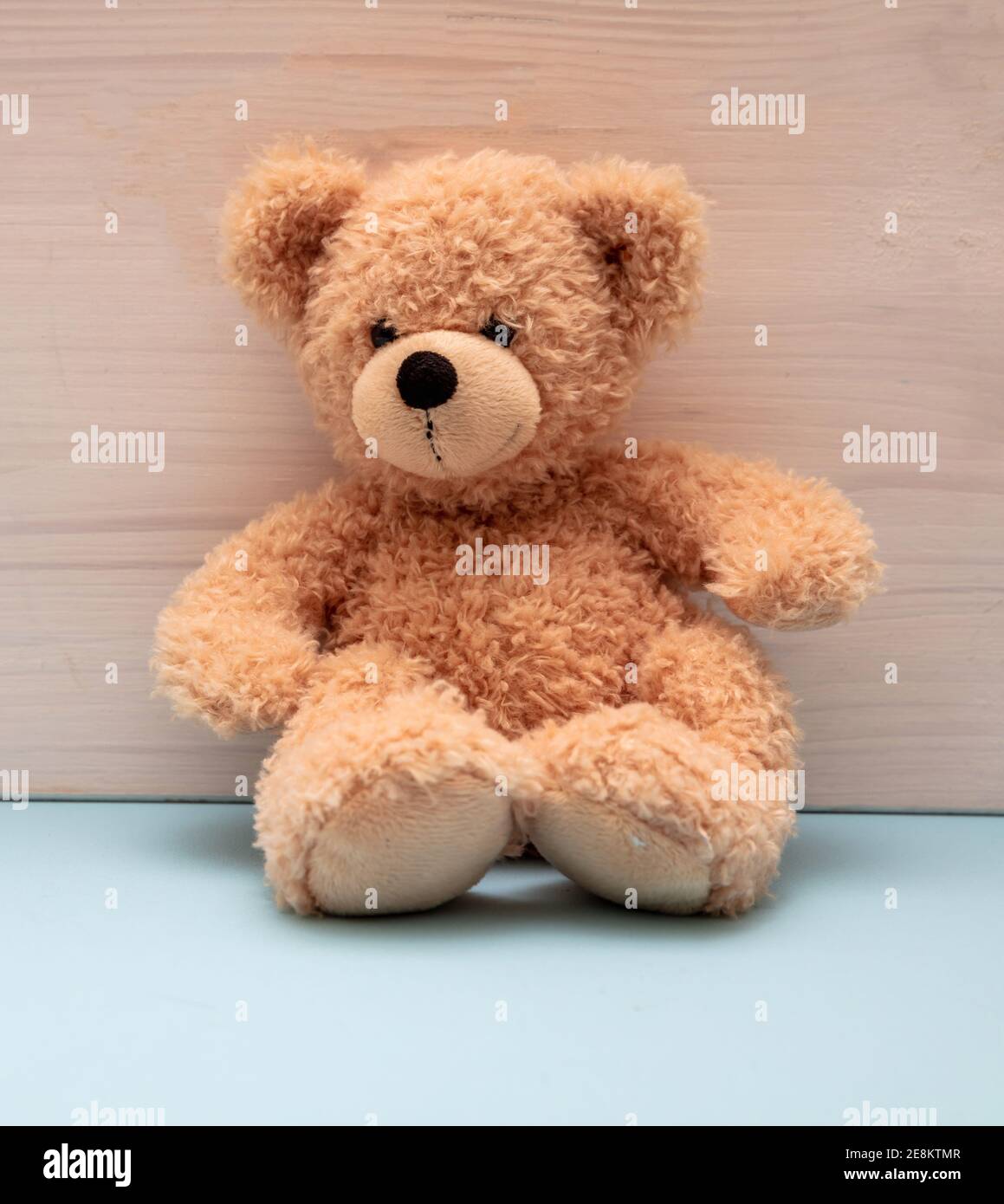 Teddybär sitzt auf pastellblauem Boden, Holzwand Hintergrund, Kinderzimmer Interieur, Kind allein Konzept Stockfoto