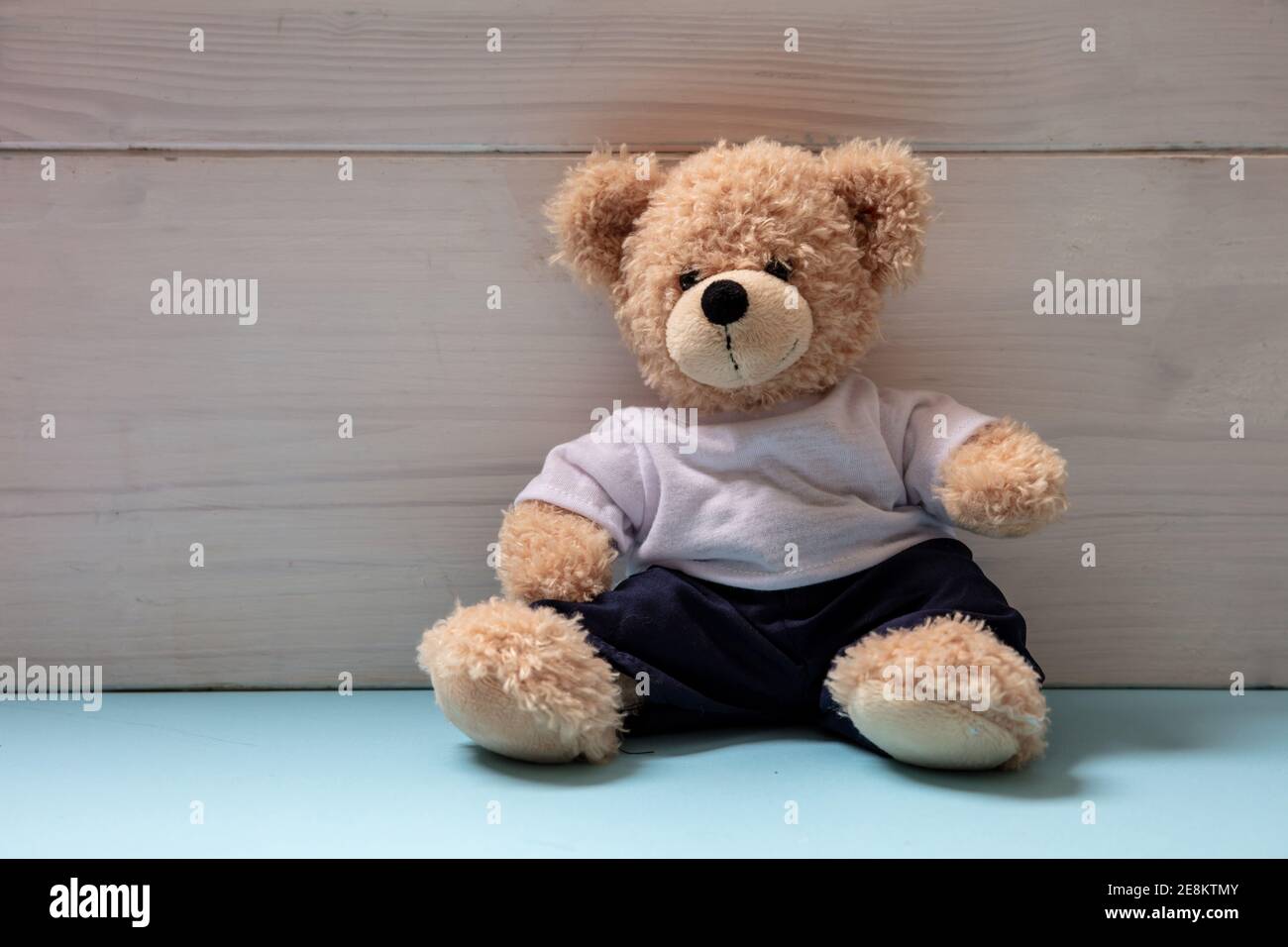 Teddybär trägt blaue Hose und weißes T-Shirt sitzt in einem leeren Raum, Kid Alone Konzept Stockfoto