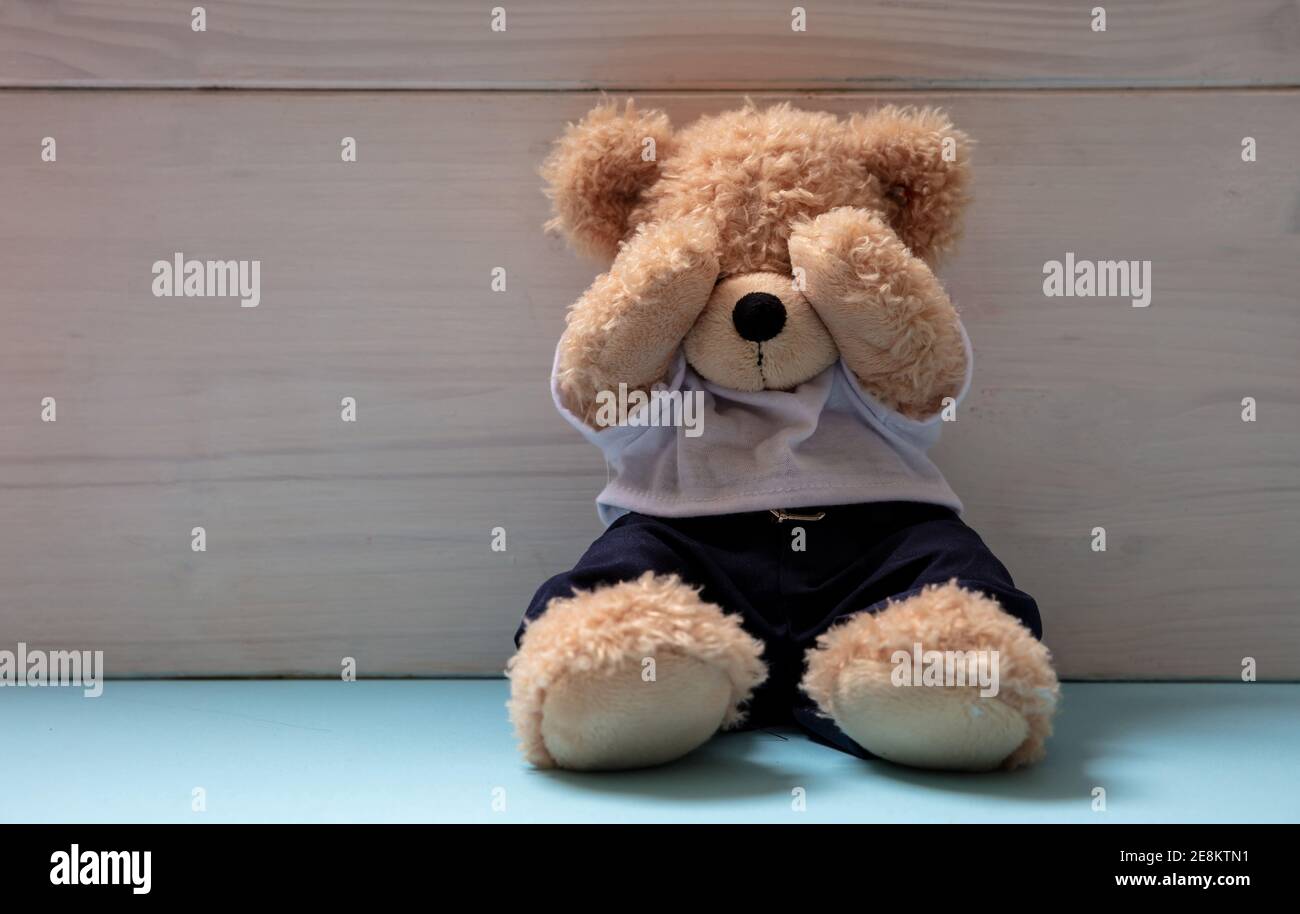 Konzept für Kindesmissbrauch. Teddybär sitzt auf blauem Boden in einem leeren Kinderzimmer, bedeckt die Augen, Kopierraum Stockfoto
