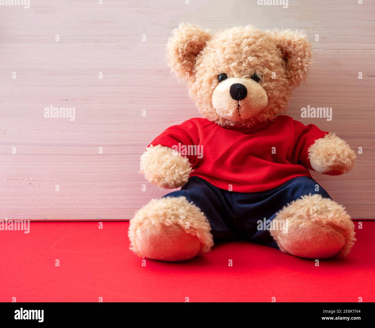 Teddybär trägt blaue Hose und weißes T-Shirt sitzt in einem leeren Raum, Kid Alone Konzept Stockfoto