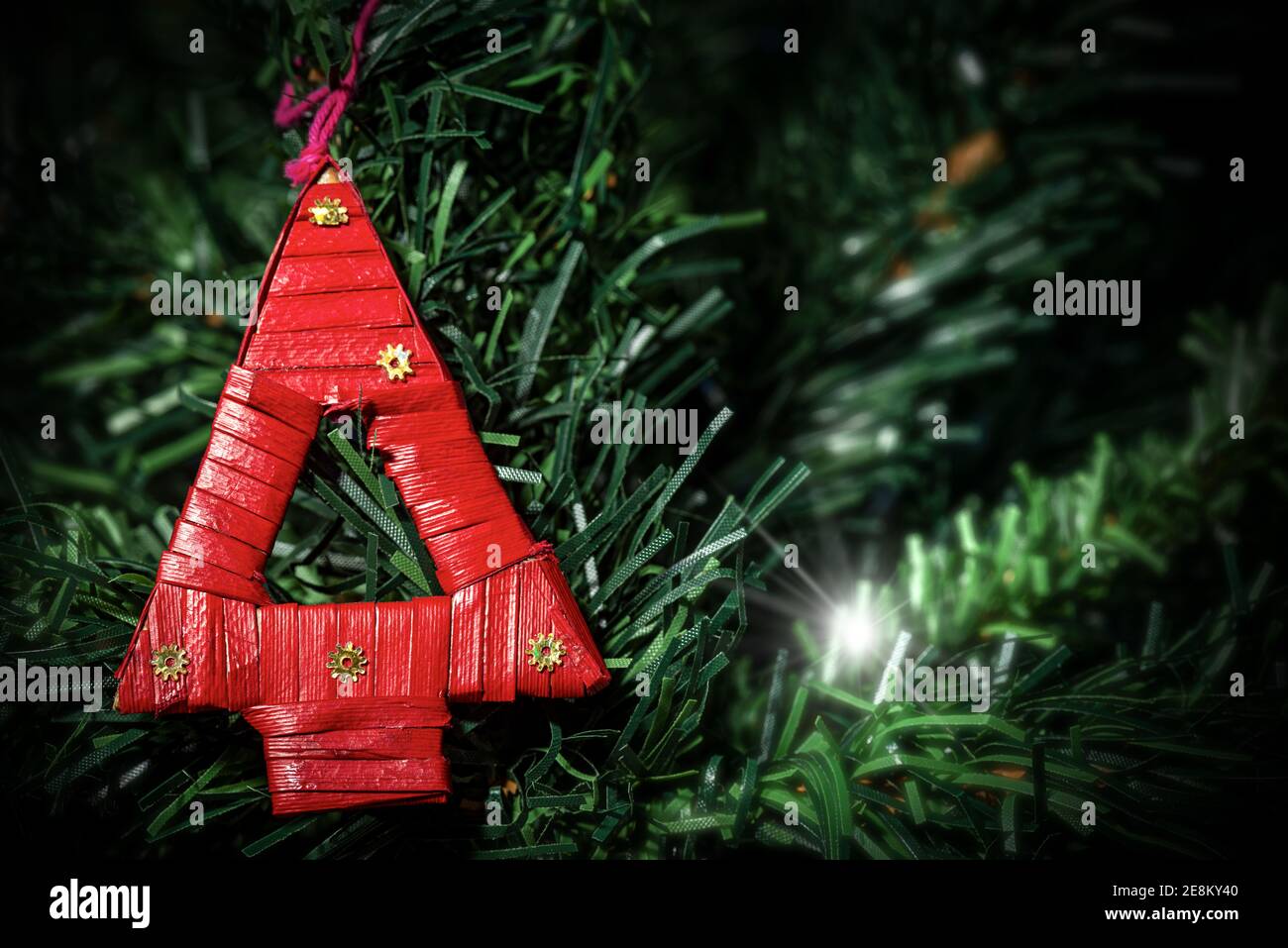 Extreme Nahaufnahme eines kleinen und roten Weihnachtsbaums aus gewebtem Stroh, der an einem grünen Weihnachtsbaum hängt. Stockfoto