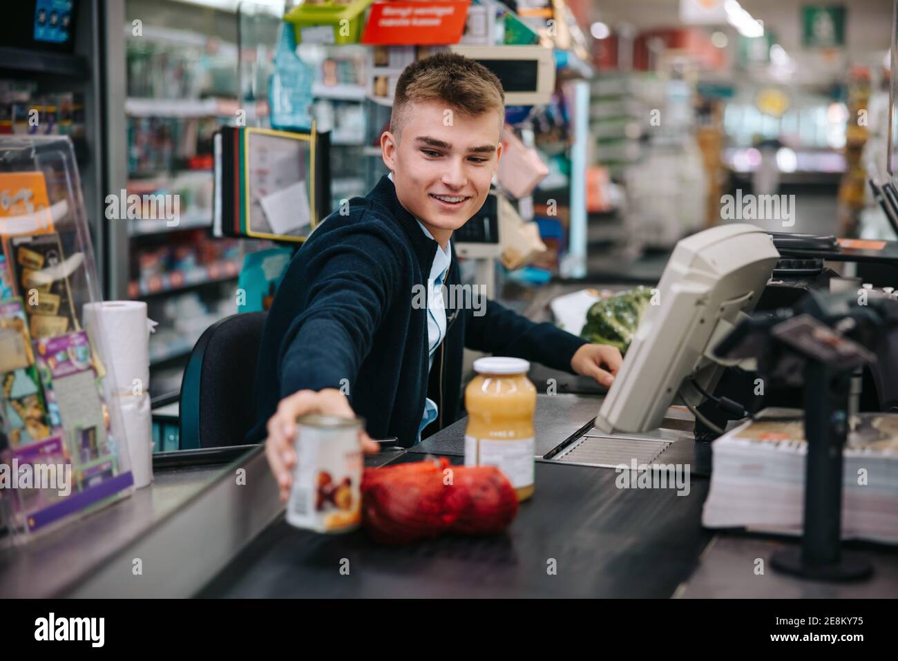 Mann, der Kunden an der Kasse im Supermarkt bedient. Männlicher Verkäufer scannt Produkte an der Kasse des Lebensmittelladens. Stockfoto