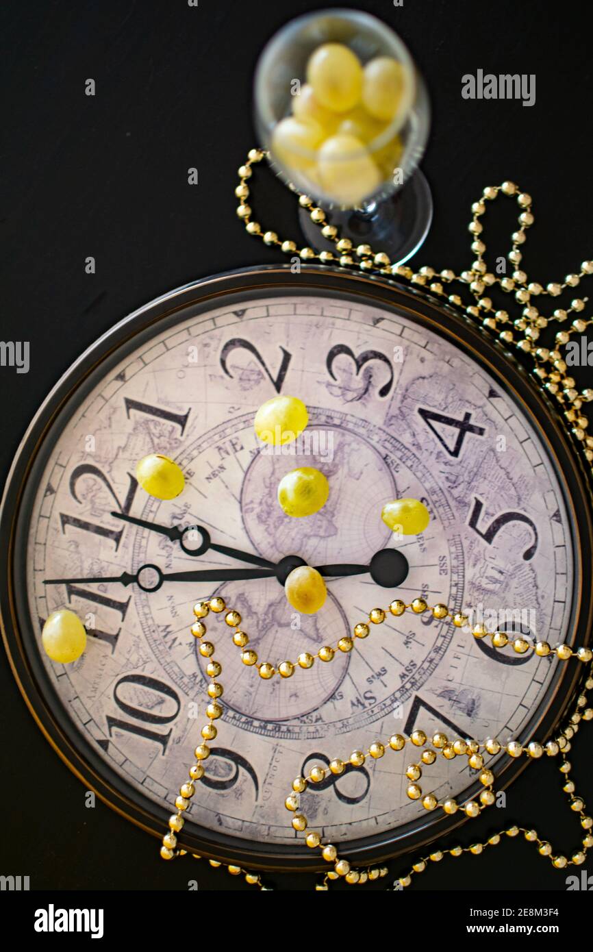 Eine Uhr, die nur wenige Minuten vor dem neuen anzeigt Die Jahre kommen neben zwölf Trauben Stockfoto