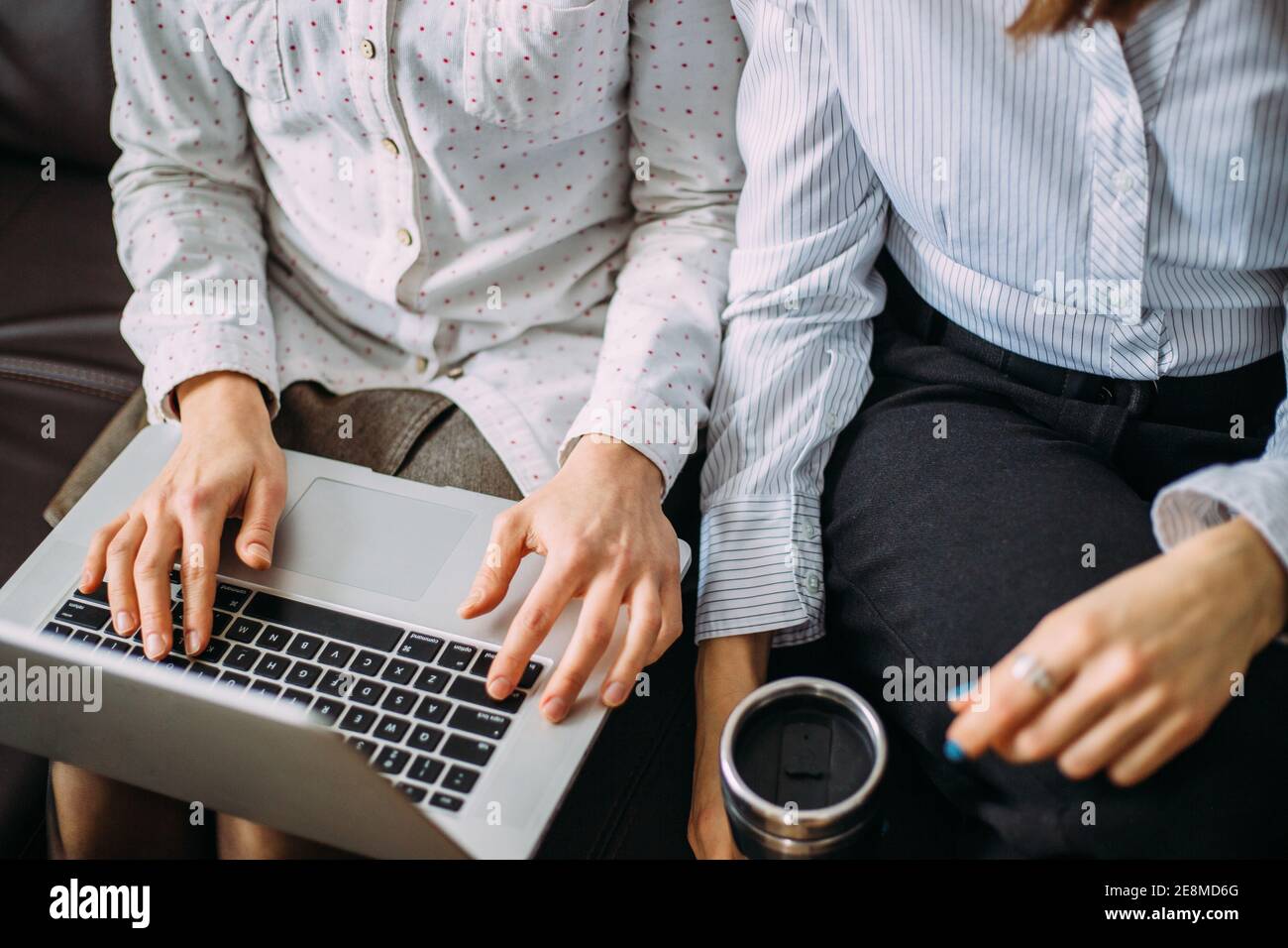 Zwei Mädchen arbeiten nebeneinander im Büro auf einem Laptop. Interaktion von Kollegen bei der Arbeit. Die Psychologie der Arbeitsbeziehungen Stockfoto