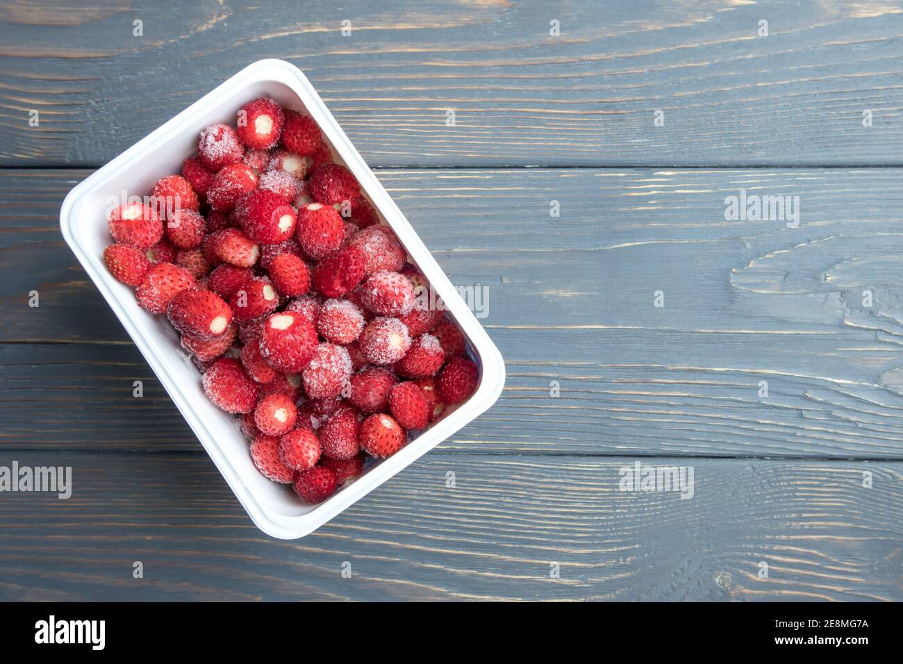 Gefrorene Erdbeeren in einem Behälter auf einem hölzernen Hintergrund mit Platz für Text. Stockfoto